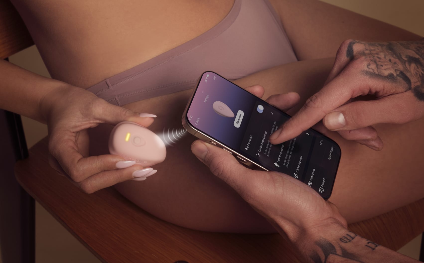 Two hands set a pink LuxHer vibrator from a phone app