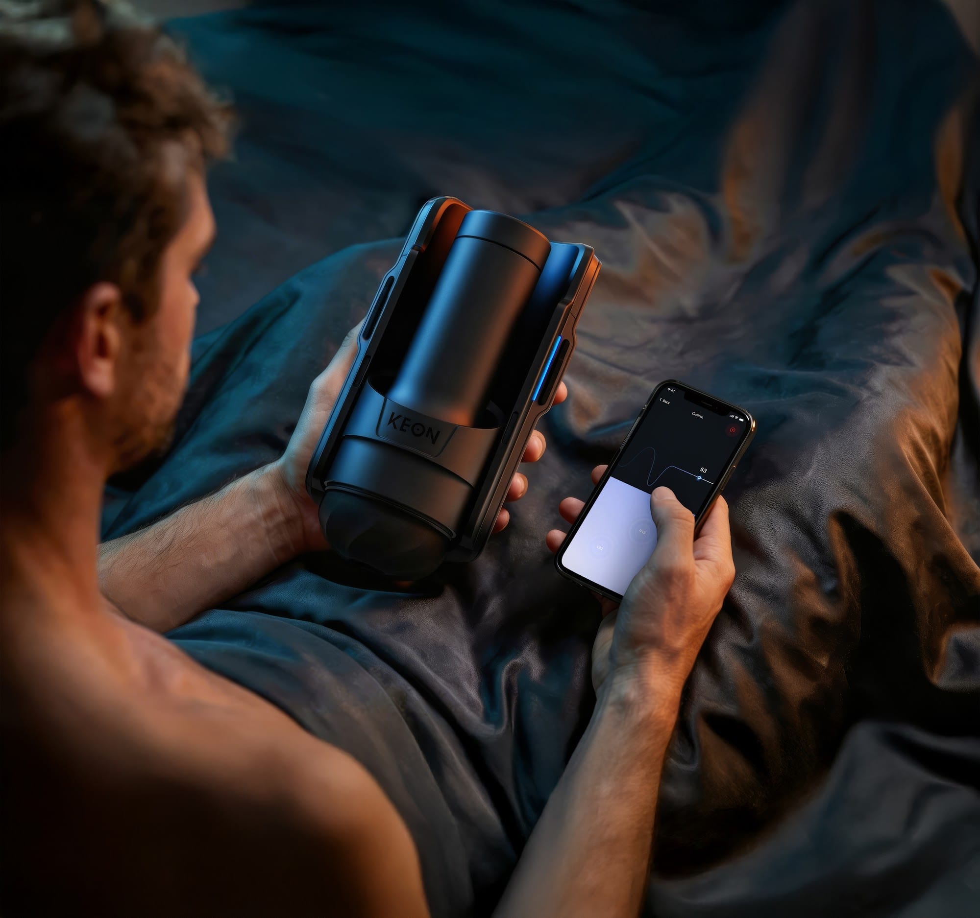A man in bed holds a Kiiroo Keon 2 and adjusts it from his phone