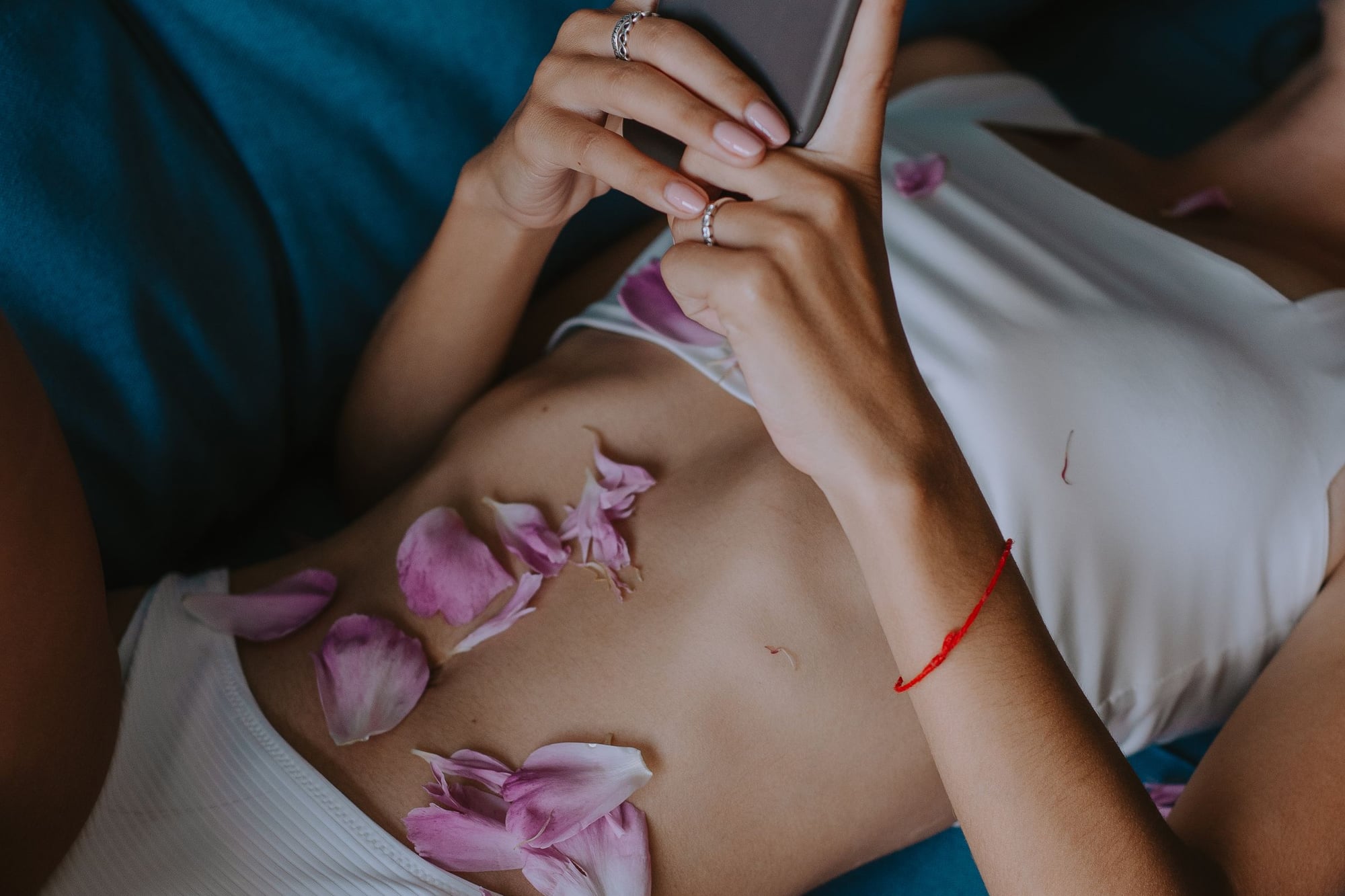 In white lingerie with petals on her skin, a phone in her hands