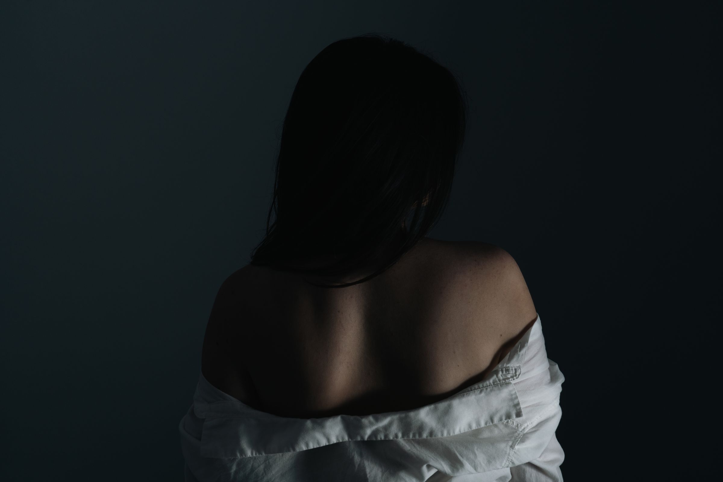 Her bare back, a white shirt sliding off her shoulders, in cold blue light