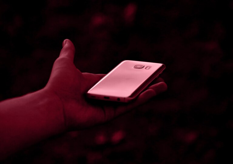 Une main tient un téléphone dans le noir, sous une lumière rouge